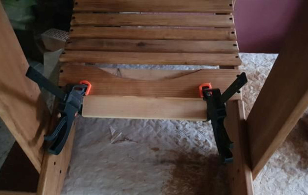 A cross slat is being clamped to the lower part of a wooden chair using clamps.