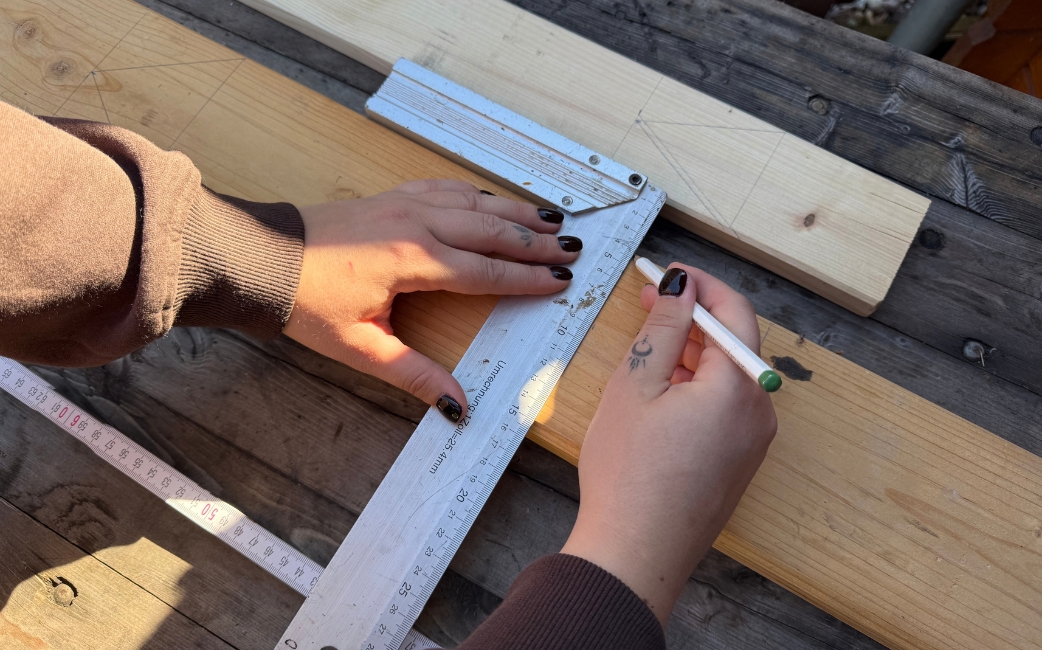 Eine Person markiert ein Holzbrett mit einem Bleistift, wobei sie ein Winkelmaß und einen Zollstock verwendet.