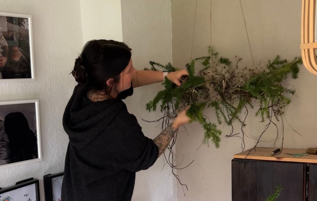 The woman attaches more branches to the hanging Advent wreath made of twigs and natural materials.