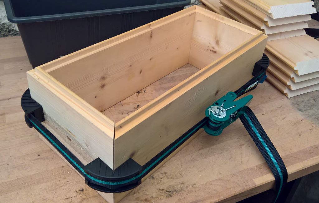 A rectangular wooden box is being assembled on a workbench using clamps.