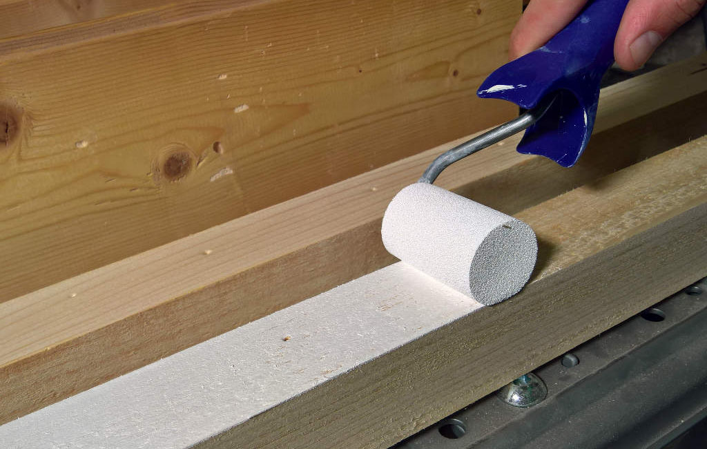A hand is applying white paint to a wooden slat using a small paint roller.