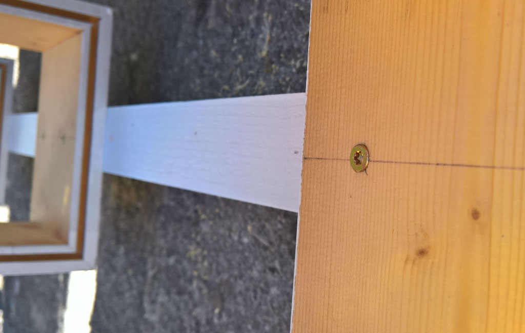 A vertical, white-painted wooden board is being screwed to a wooden box.
