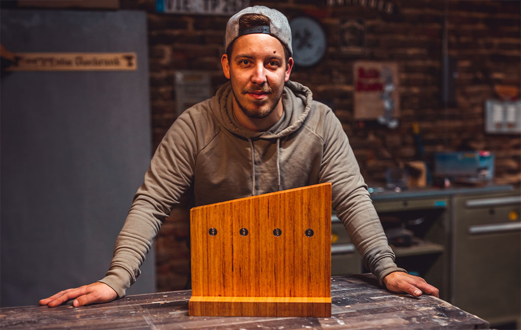 A man in a grey hoodie presents an empty wooden knife block with four magnetic spots on the back.