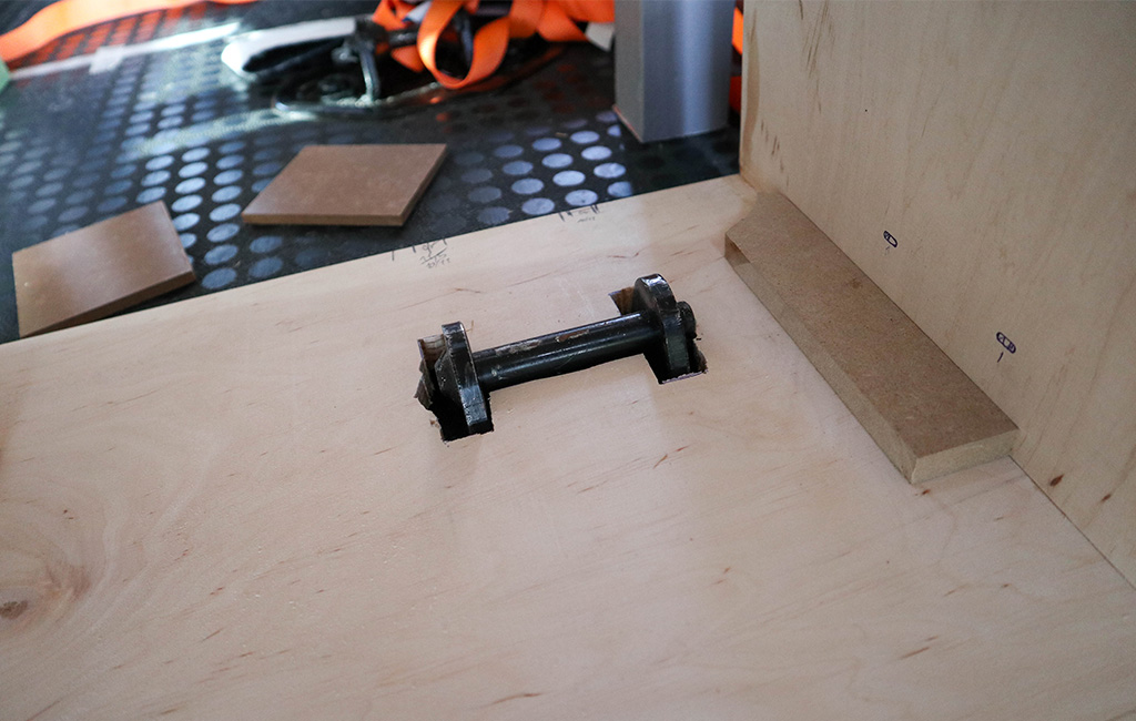 Seat anchor embedded in a wooden board inside the van, prepared for installation of the camping box.