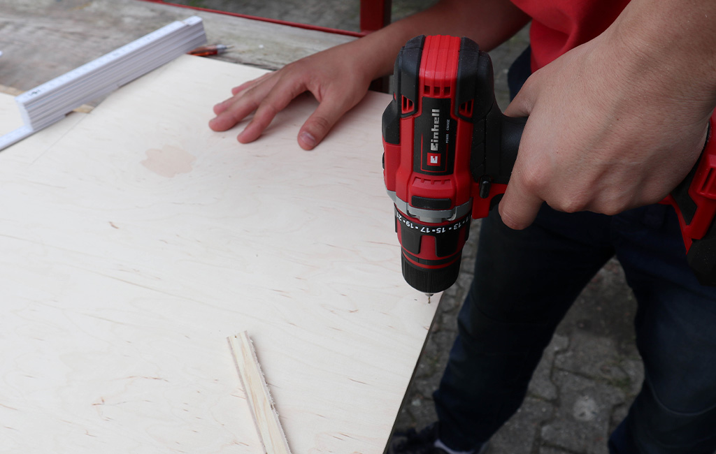Person drilling into a plywood board using an Einhell cordless screwdriver.