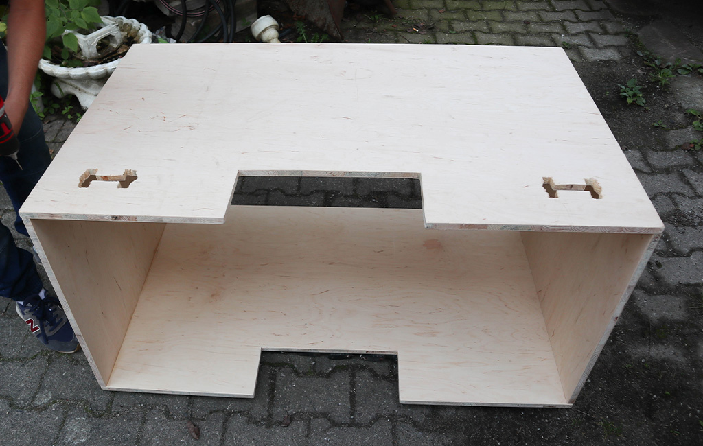 Assembled wooden cabinet with cut-outs, standing on paving stones.