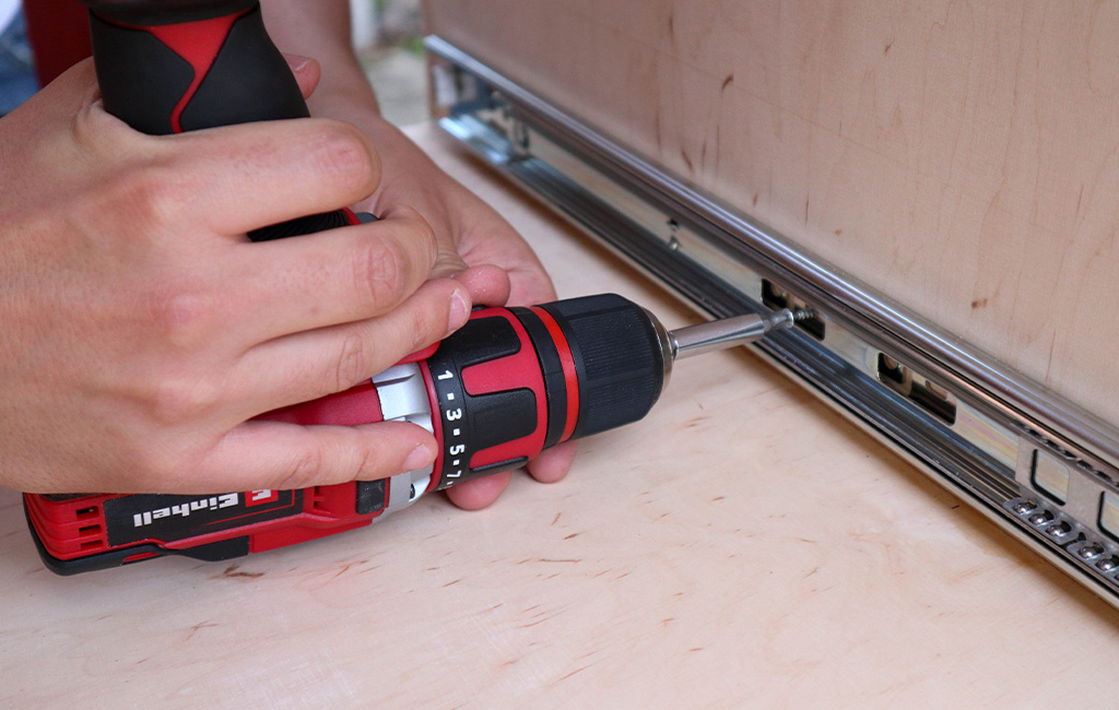Close-up of an Einhell cordless screwdriver fastening a drawer slide to wood.