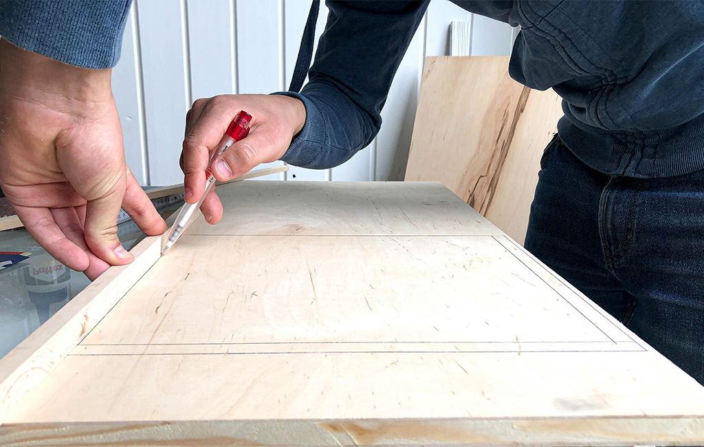 Person drawing a rectangular marking on a wooden board using a pencil and ruler.