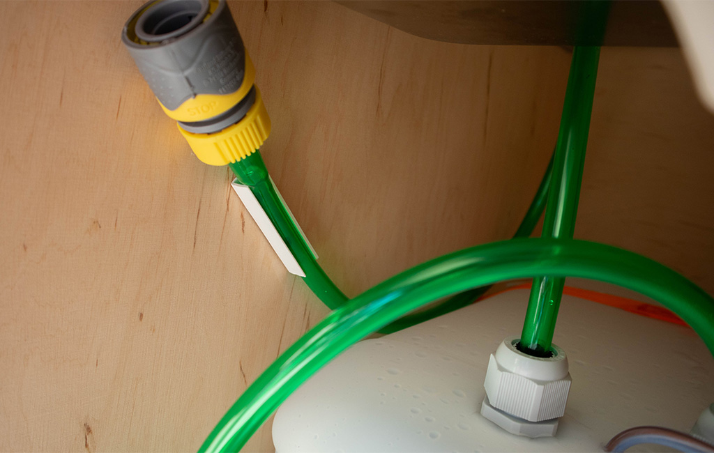 Green water hoses inside the camping box, connected to a canister.