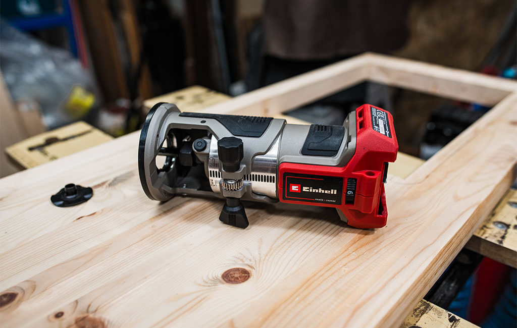 An Einhell cordless edge router lies on a milled wooden frame of the mud kitchen.