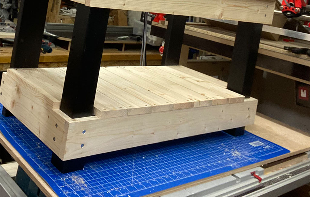 The lower wooden shelf of the mud kitchen is assembled with black table legs.