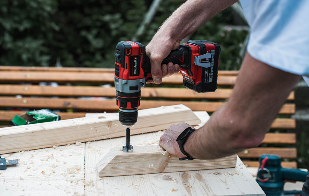 A person drills a hole into an angled piece of wood using an Einhell cordless drill.