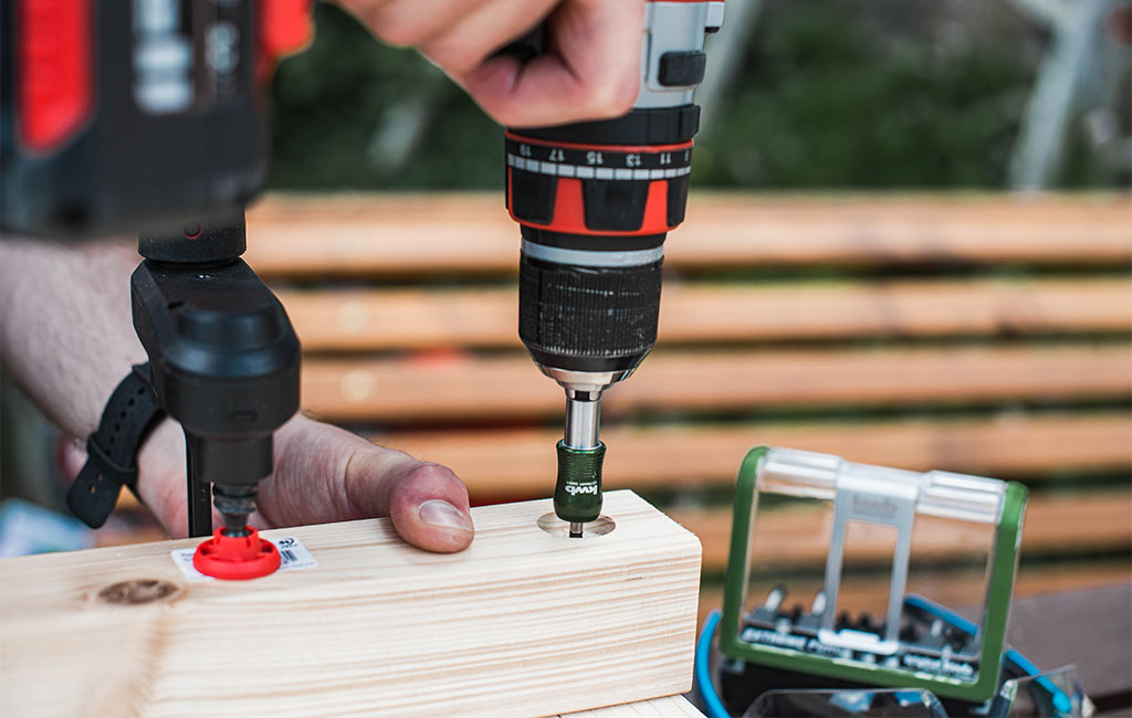 Close-up: A cordless drill with bit attachment drives a screw into a piece of wood.