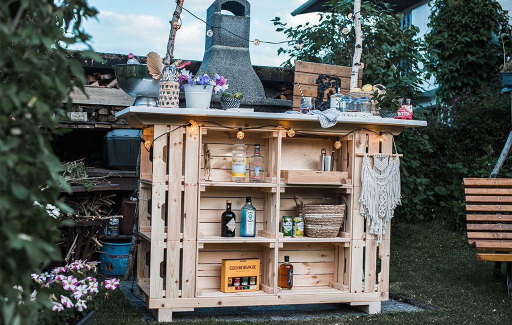 The finished DIY garden bar stands decorated with drinks and plants in a garden.