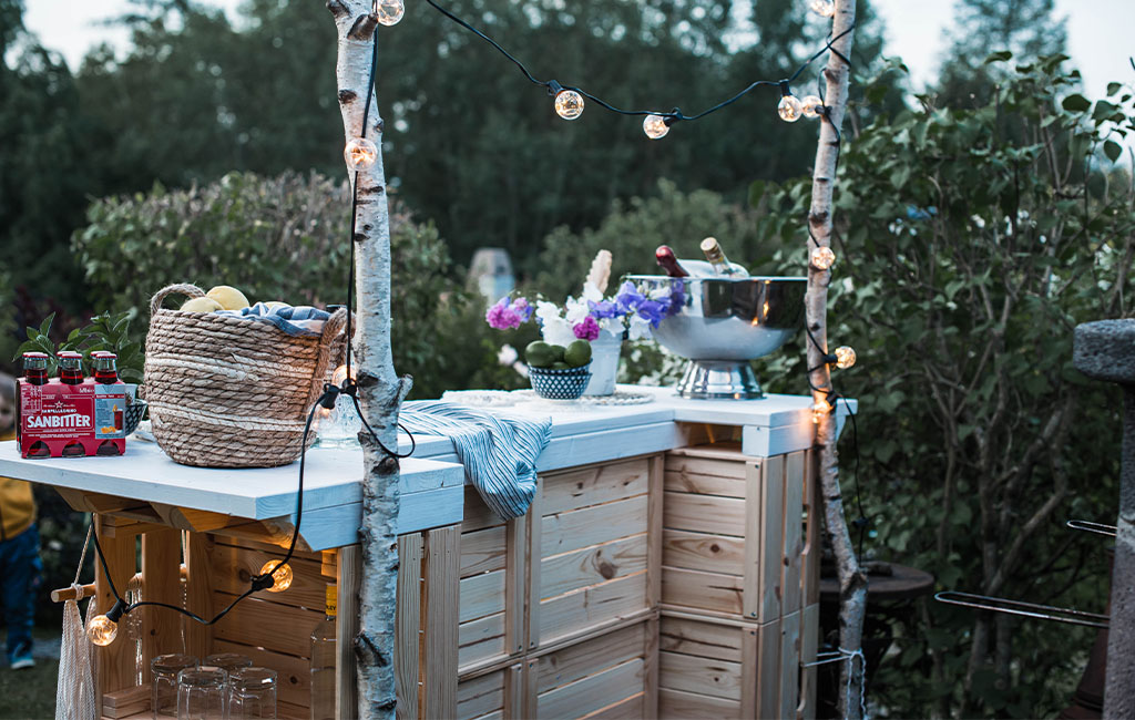 Backside of the bar with string lights, drinks, flowers, and two birch poles as decoration.