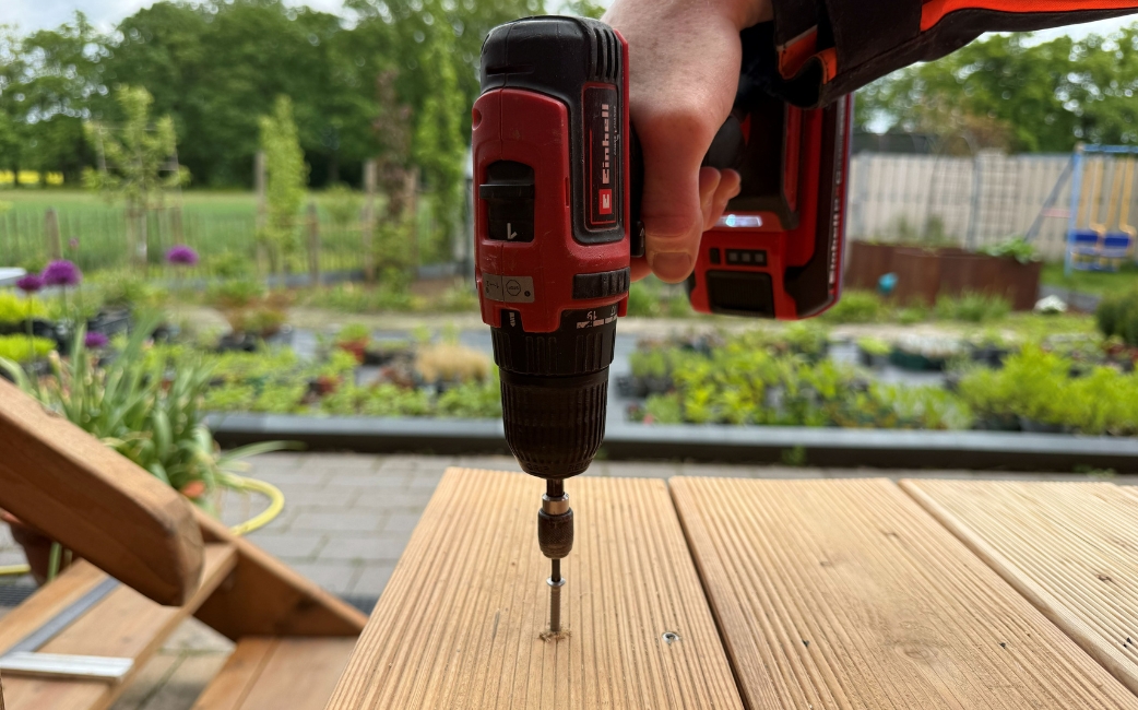 Ein Akku-Bohrschrauber bohrt Löcher in die Holzbretter für die Rückwand des Pflanztisches vor.