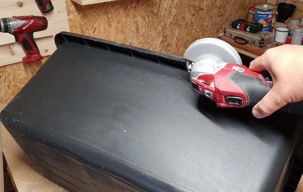 Eine Hand hält einen Einhell Winkelschleifer und schneidet den Rand einer schwarzen Kunststoffbox ab.