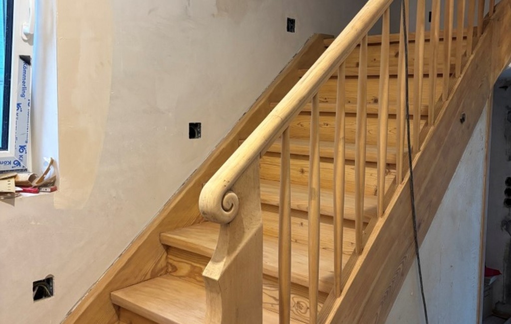 Geschliffene Holztreppe mit Geländer im Innenbereich während der Renovierung.