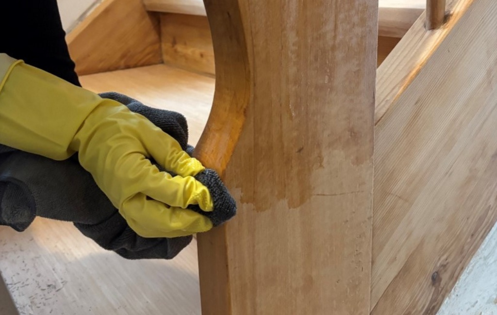 Eine Person mit gelben Handschuhen ölt das Holzgeländer einer Treppe mit einem Tuch.
