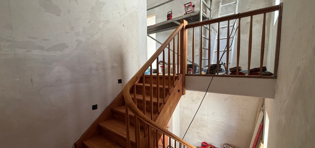 Geschliffene Holztreppe mit Geländer im Innenbereich während der Renovierung.
