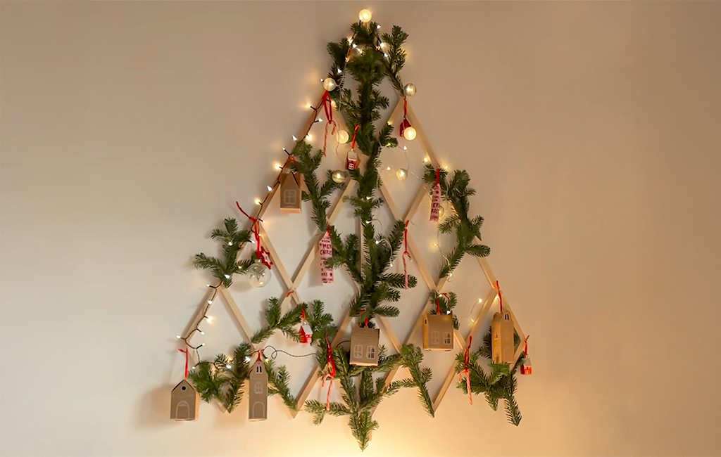 Ein dekorierter DIY-Holz-Weihnachtsbaum in Tannenbaumform mit Lichtern, Tannenzweigen und kleinen Geschenkschachteln.
