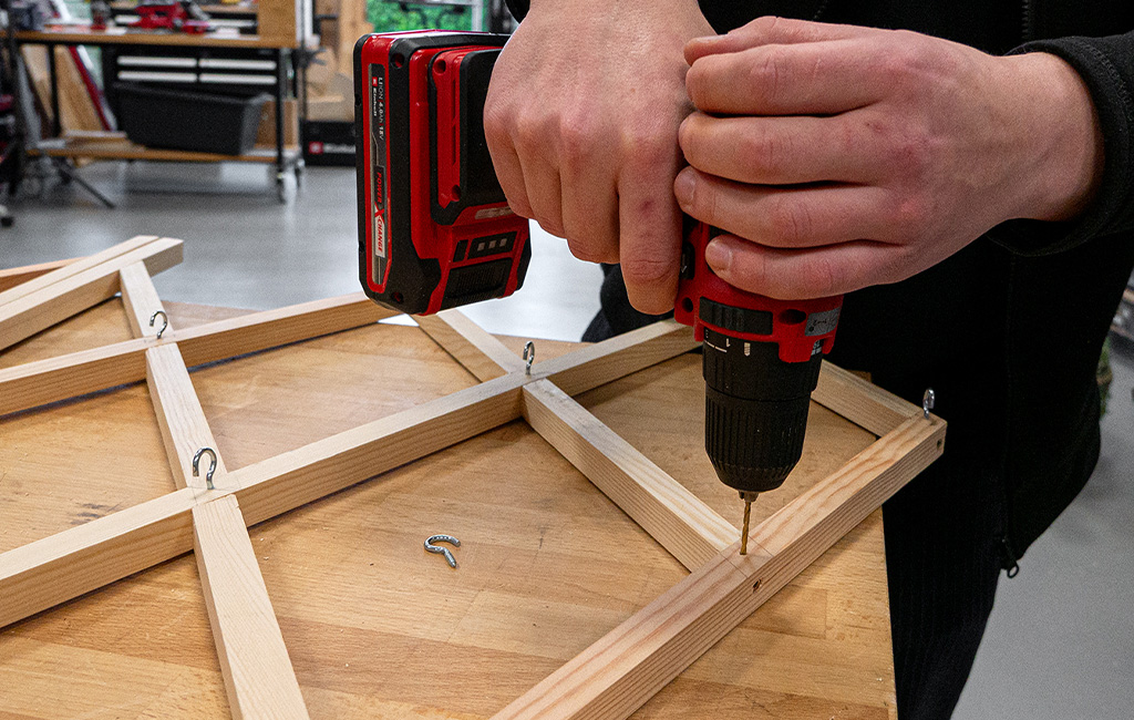 Mit einem Einhell-Akkuschrauber werden Haken in ein Holzgitter geschraubt.
