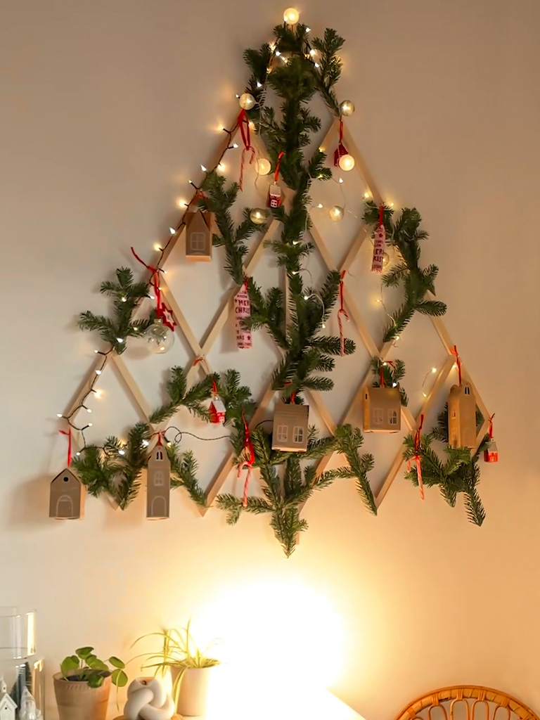 Ein dekorierter DIY-Holz-Weihnachtsbaum in Tannenbaumform mit Lichtern, Tannenzweigen und kleinen Geschenkschachteln.