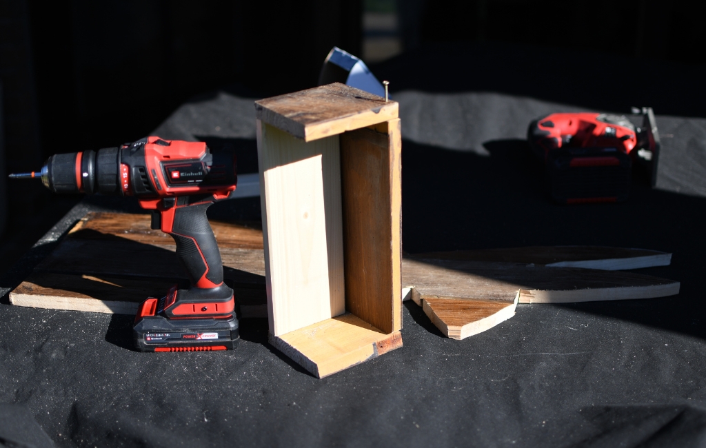 Zusammengebautes Holzgehäuse steht neben Akku-Bohrschrauber und Holzteilen auf einem Tisch.