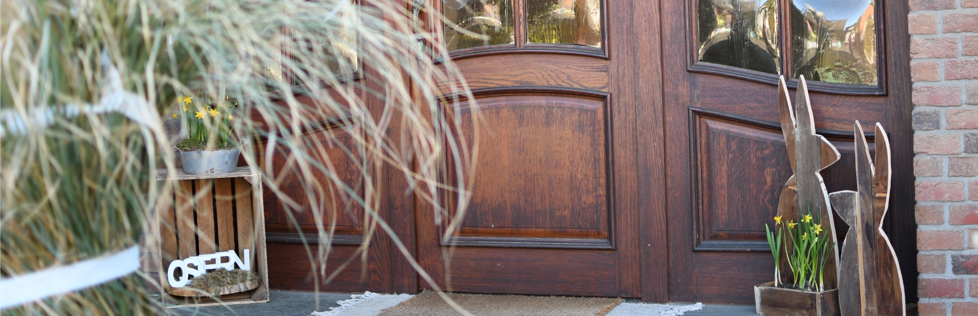 Zwei Holzhasen und eine Kiste mit gelben Blumen stehen vor einer Haustür.