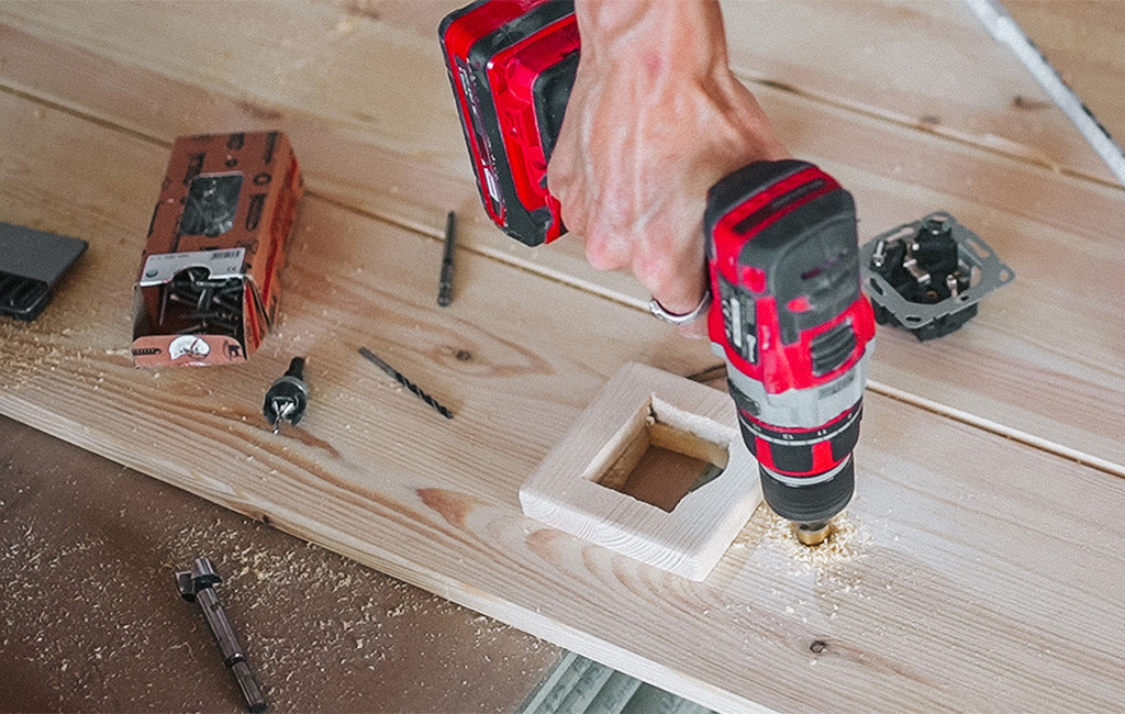 A hole saw is used to drill a cutout for the socket in the wooden beach chair.