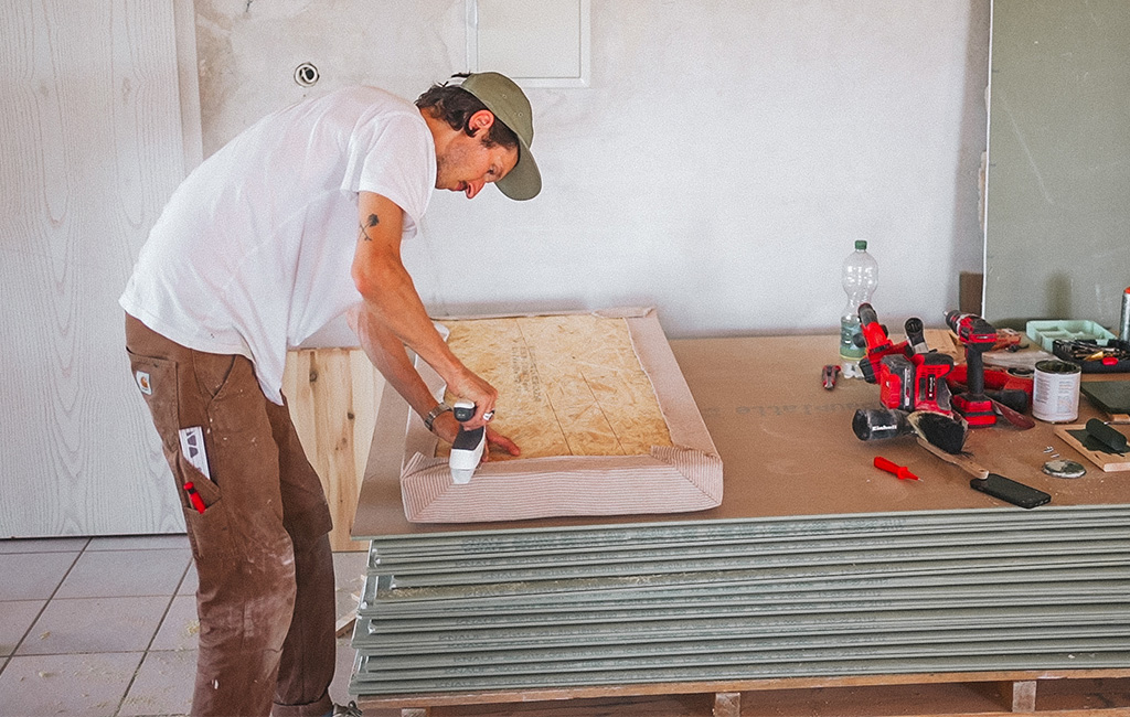 A man staples fabric around a cushion for the self-made wooden beach chair.