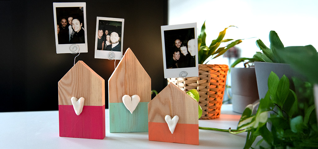 Three decorated wooden photo holders with instant photos stand among houseplants.