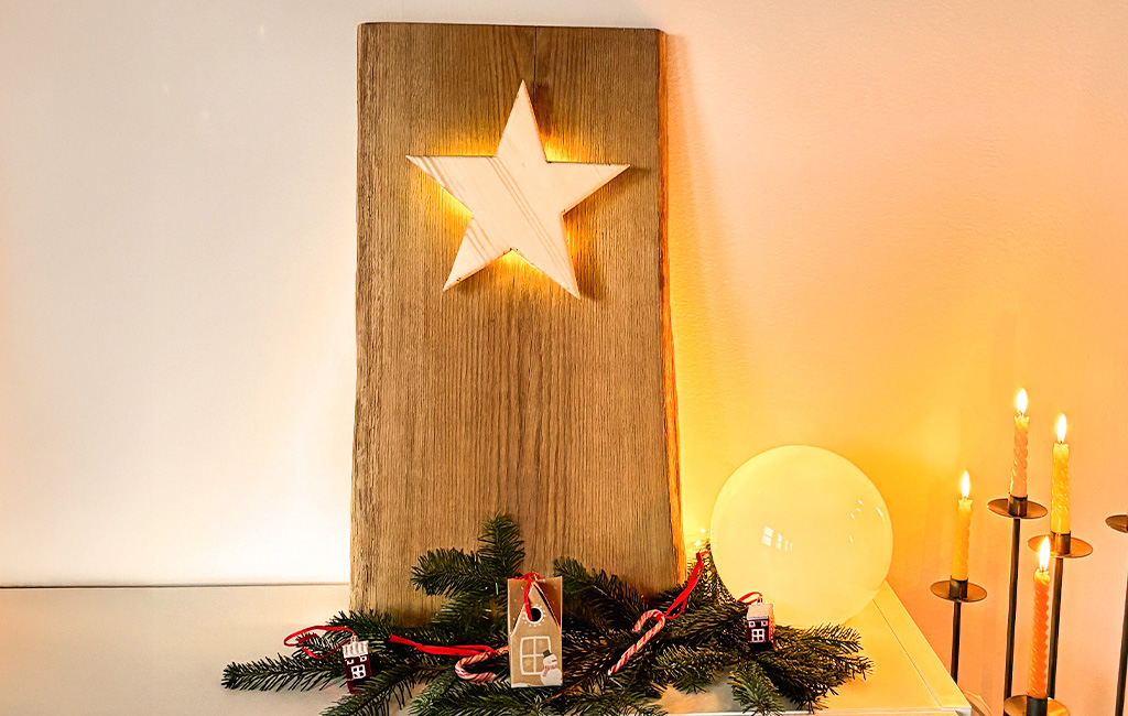 Ein beleuchteter Holzstern ist in eine große Holzplatte eingelassen, dekoriert mit Tannenzweigen und Kerzen.