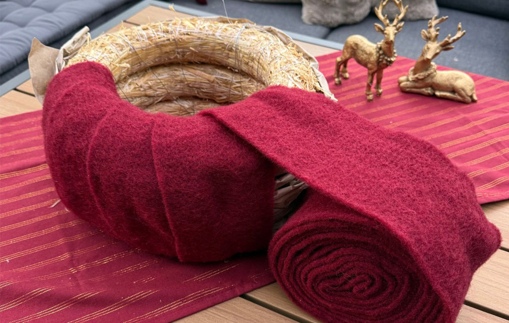A straw wreath is being wrapped in red felt, with a large roll of felt beside it.