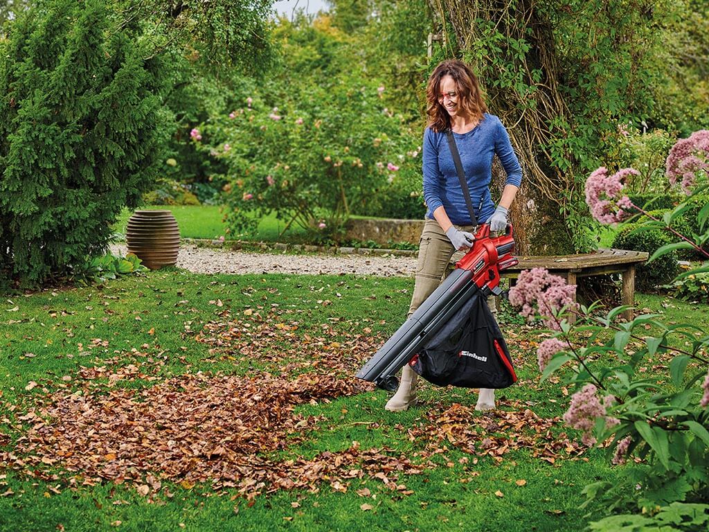 A woman in the garden vacuuming up autumn leaves with an Einhell cordless leaf vacuum.