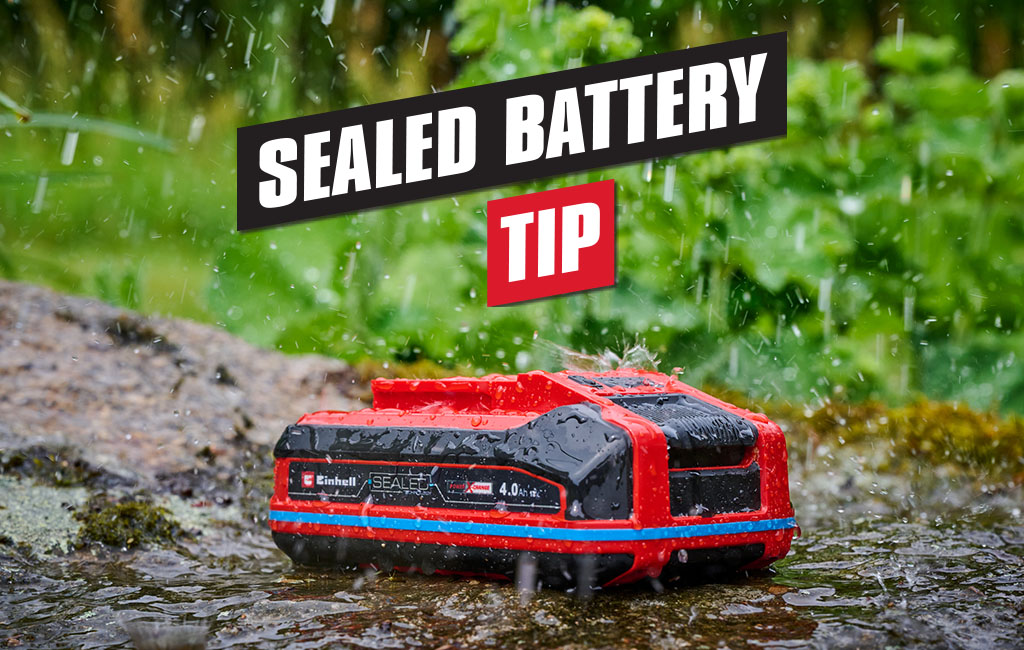 A weatherproof Einhell SEALED battery lies on a stone in the rain.