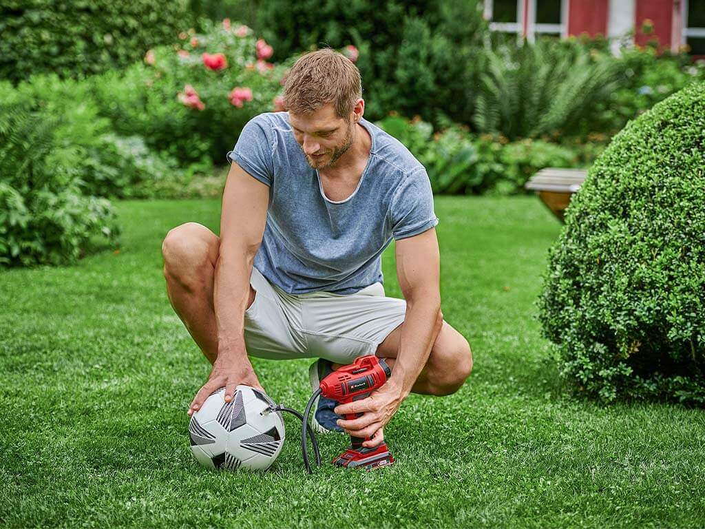 A man pumps up a football with the Einhell cordless car compressor.