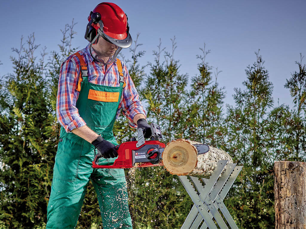 A man sawing through a thick tree trunk with the help of a cordless chainsaw from Einhell.