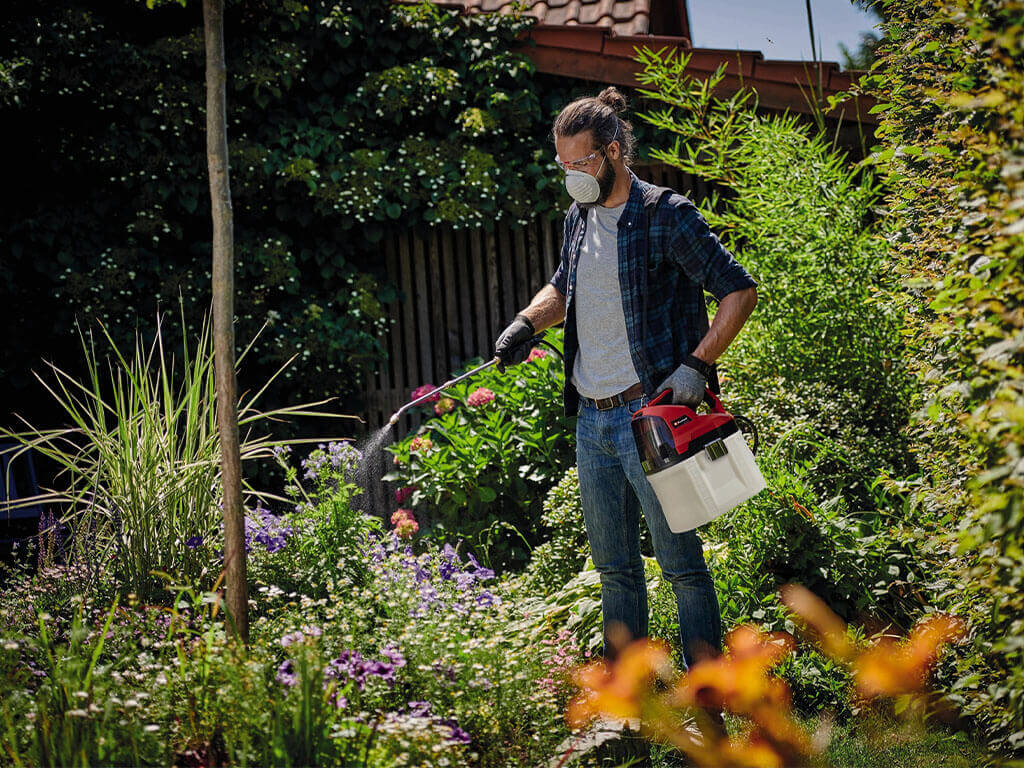 A man sprays weedkiller in his garden with an Einhell pressure sprayer