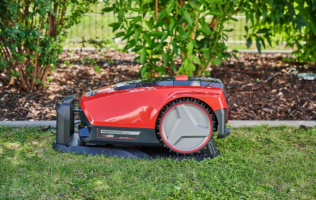 Ein rot-schwarzer Mähroboter in einer Ladestation im Garten.