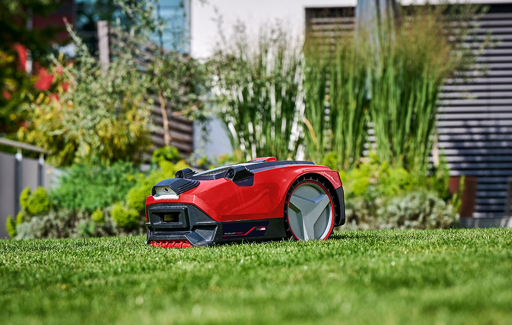 Ein Mähroboter mit Kamera- und Sensortechnik steht auf dem Rasen in einem Garten.