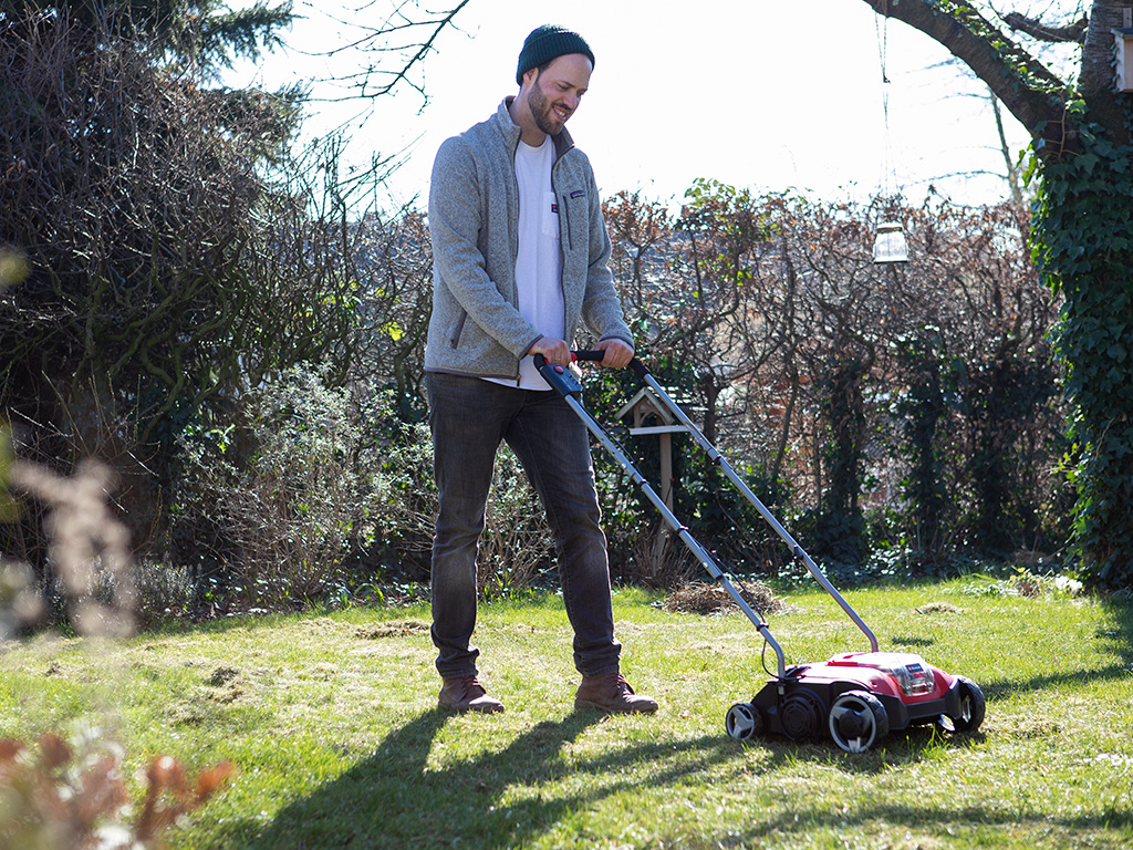 A man using a cordless scarifier on the lawn in his garden.