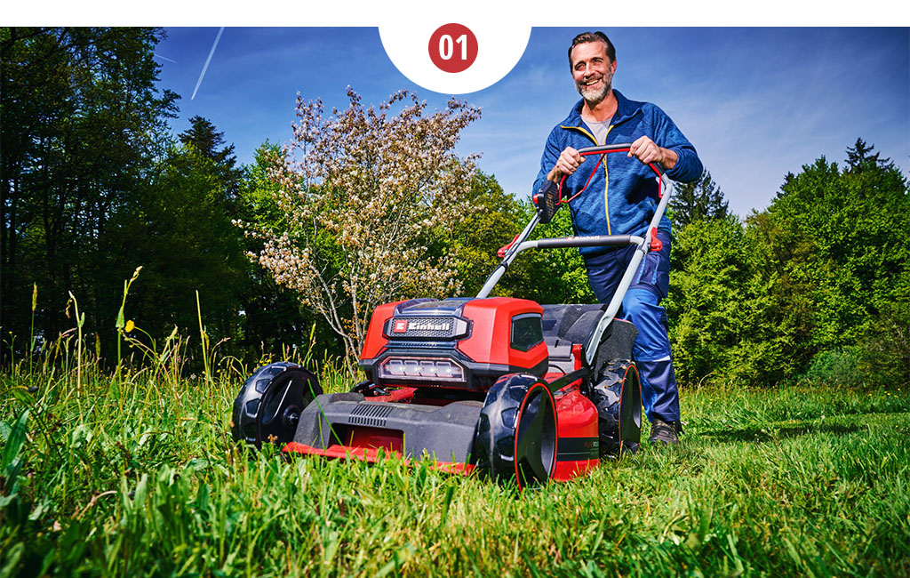 A man mowing the lawn with a large Einhell cordless lawn mower.