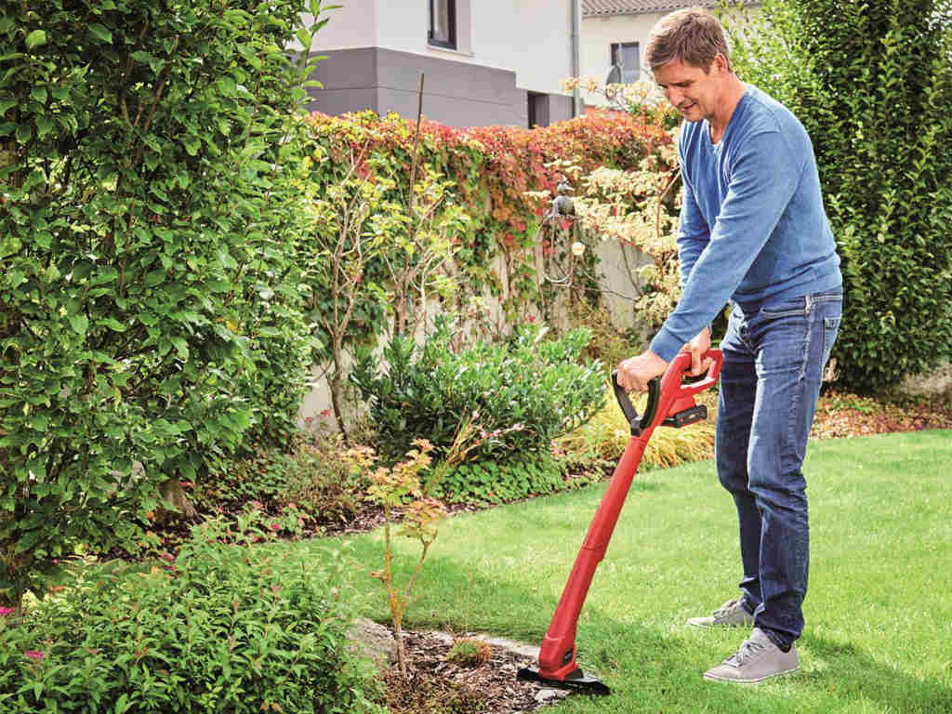 A man trims the edges of the lawn in a garden with a cordless lawn trimmer from Einhell.