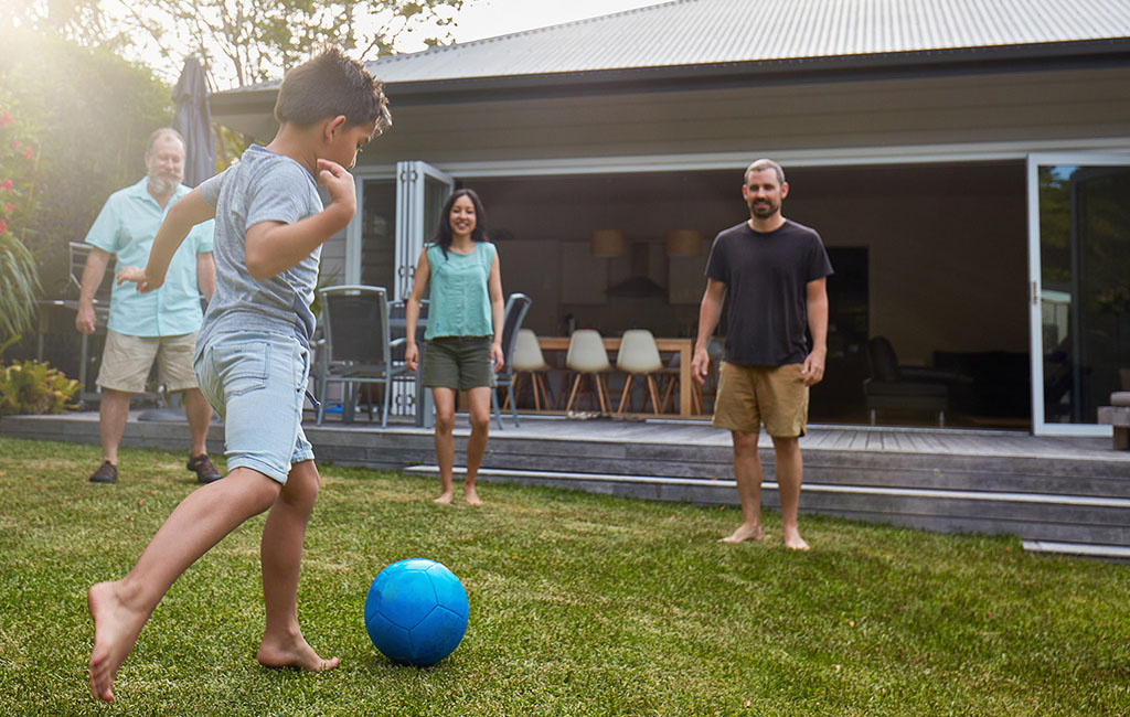 Three adults and a child playing soccer together in a garden