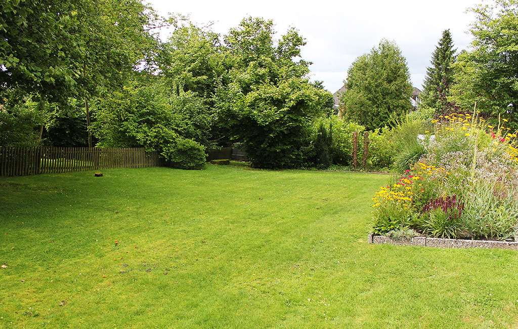 Picture of a garden with a flower bed and trees in the background.