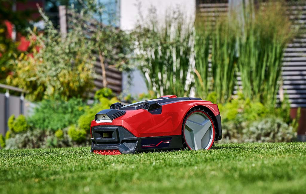 A robot mower from Einhell mows a well-kept lawn. A modern house can be seen in the background.