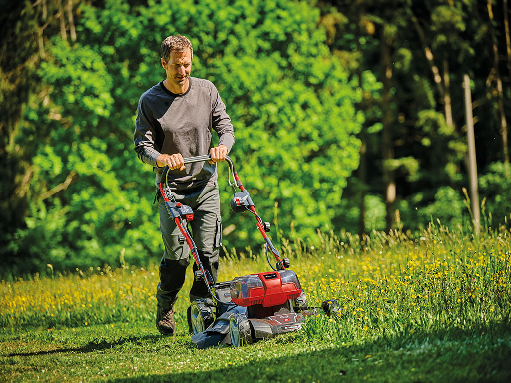 Ein Mann mäht und mulcht eine große Rasenfläche mit einem Akku-Rasenmäher mit Seitenauswurf.
