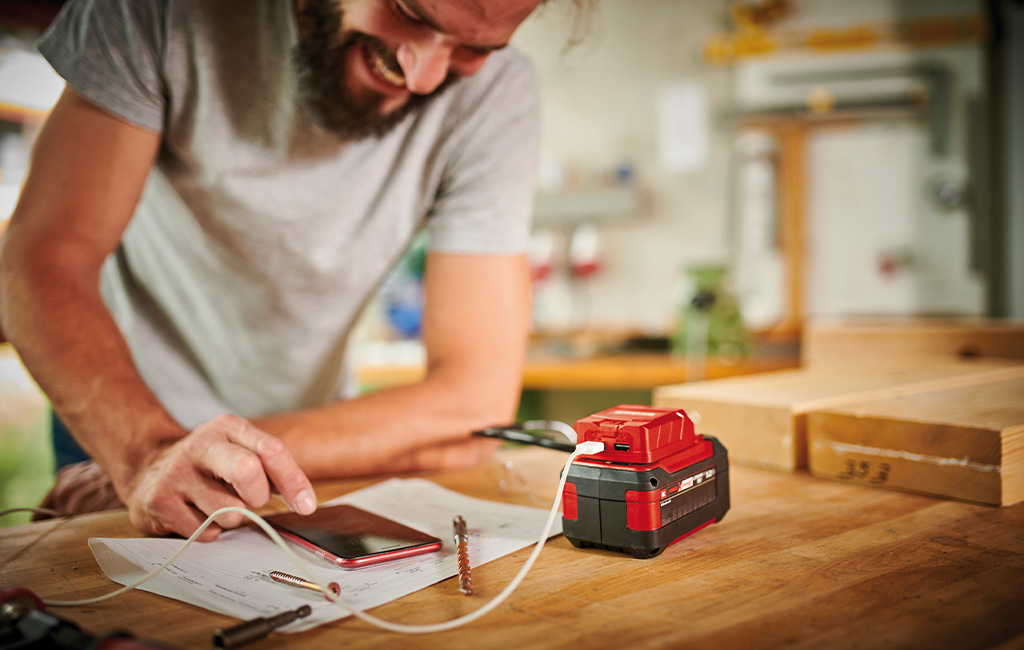 A man uses the Einhell USB battery adapter with a PXC battery to charge his cell phone.