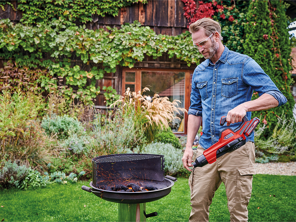 A man is using the einhell cordless blower to light the grill